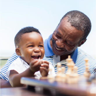 Grandfather and infant grandchild play with chess pieces.